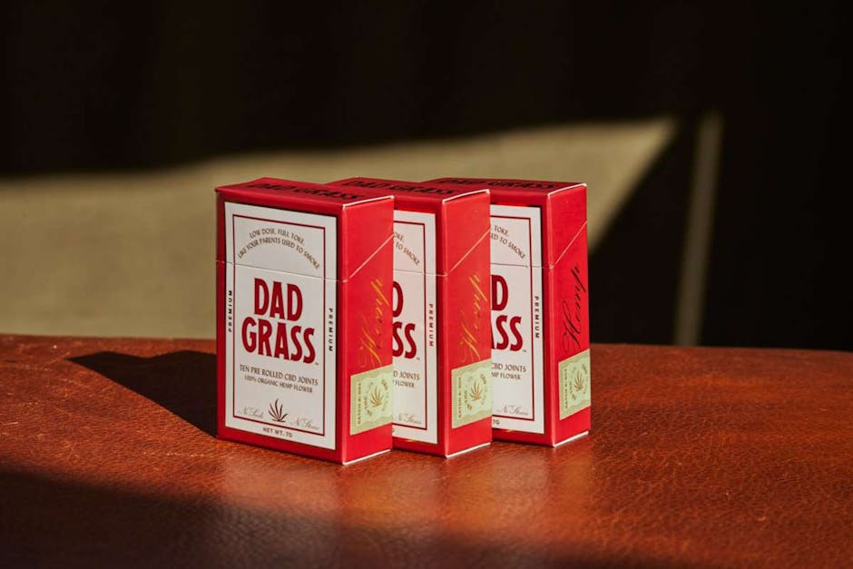 Three red CBD joint boxes placed on a leather surface in natural light.