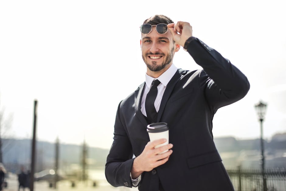 Smiling businessman in formal attire with coffee cup enjoying a sunny day outdoors.