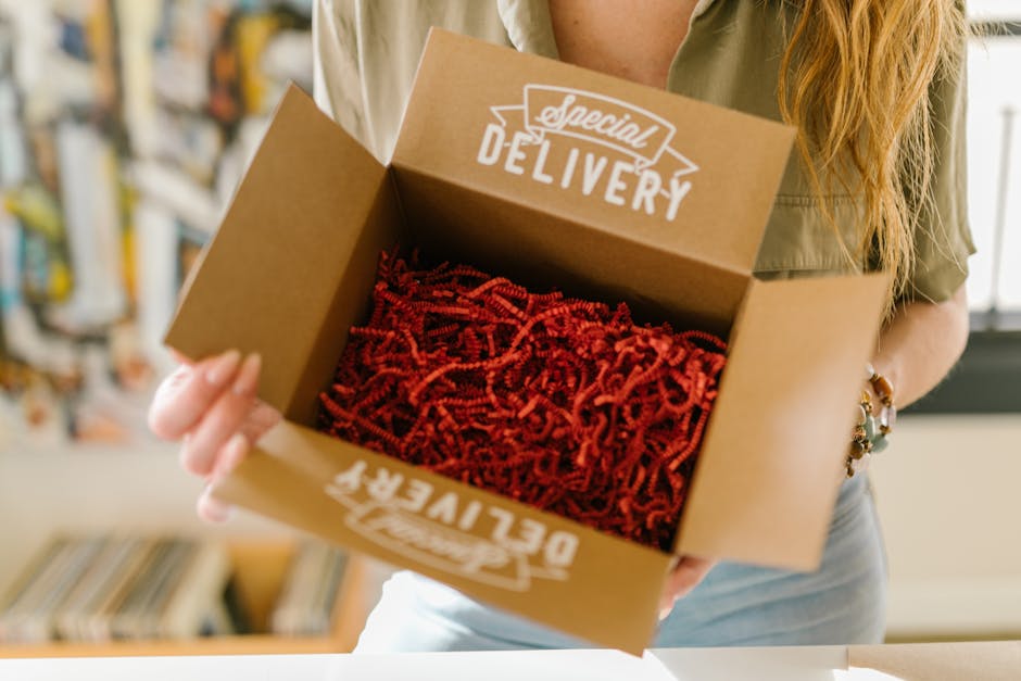 Person opening a special delivery box filled with red crinkle paper for secure packaging.