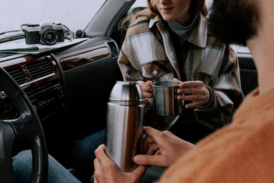 A couple sits inside a car, holding a thermos and cups, enjoying a cozy moment.