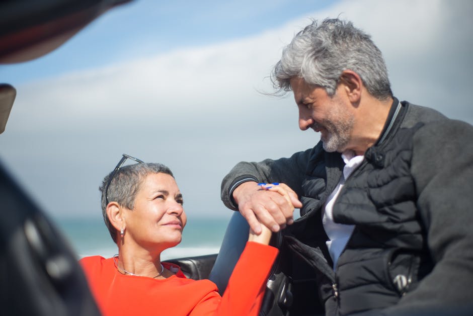 Smiling couple holding hands and looking at each other by the ocean, showcasing love and connection.