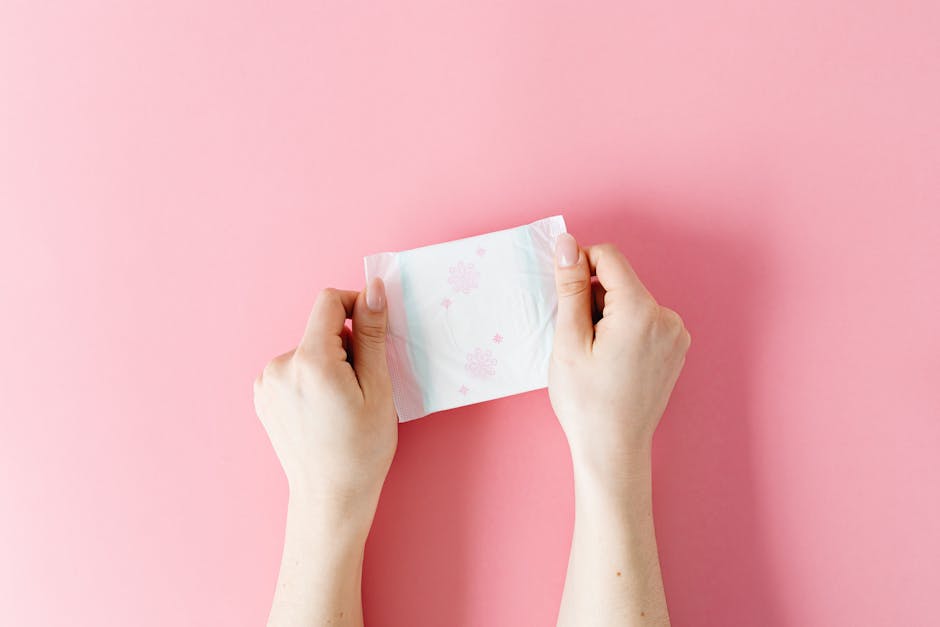 Close-up of hands holding a sanitary pad on a pink background, symbolizing hygiene and care.