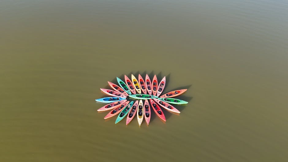 Drone view of multicolored kayaks forming a circle on calm lake waters.