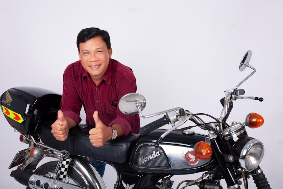 Middle-aged man giving thumbs up next to a vintage motorcycle in a studio setting.