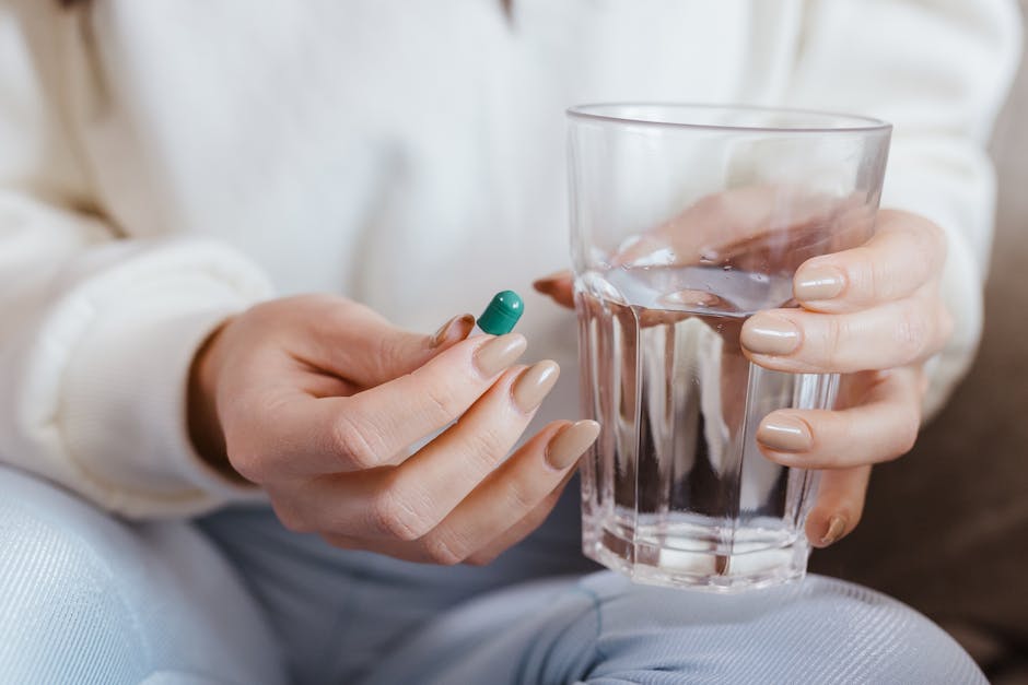 Adult woman hands holding a pill and a glass of water, ready to take medication.
