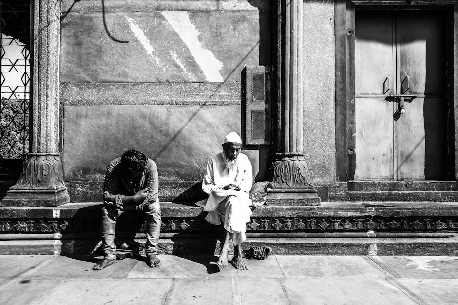 Black and white street portrait capturing two men in deep thought against a textured wall.
