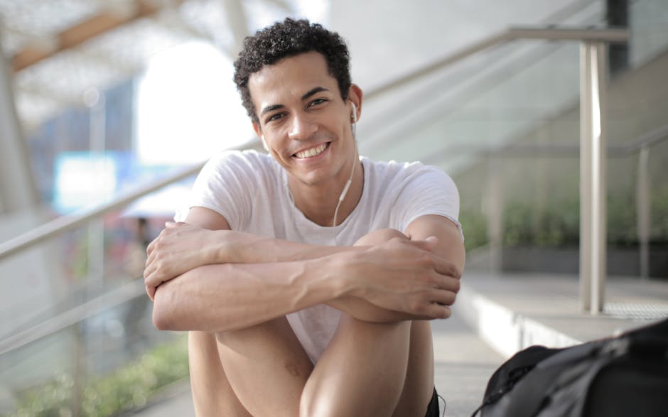 Happy young man sitting outdoors with earphones, enjoying music on a sunny day.