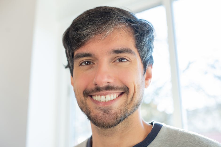 Close-up of a smiling man with a beard in natural light indoors.