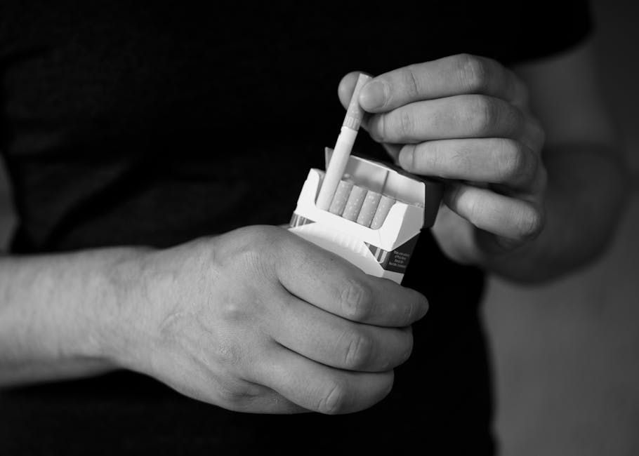 A monochrome close-up of hands holding a cigarette pack, emphasizing addiction.