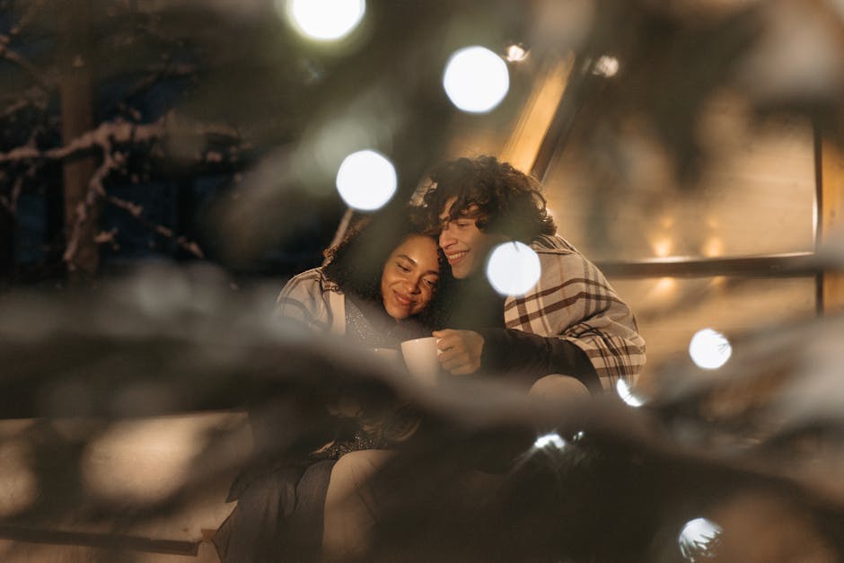 Couple enjoying a warm, romantic embrace during a winter evening with festive lights.