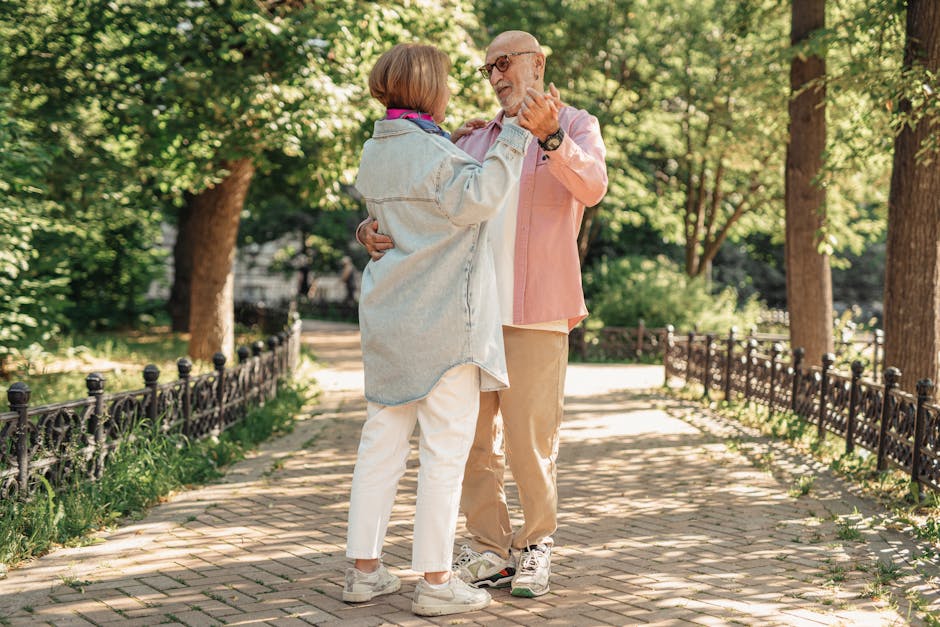 A joyful elderly couple dancing outdoors, showcasing love and happiness in a sunlit park.