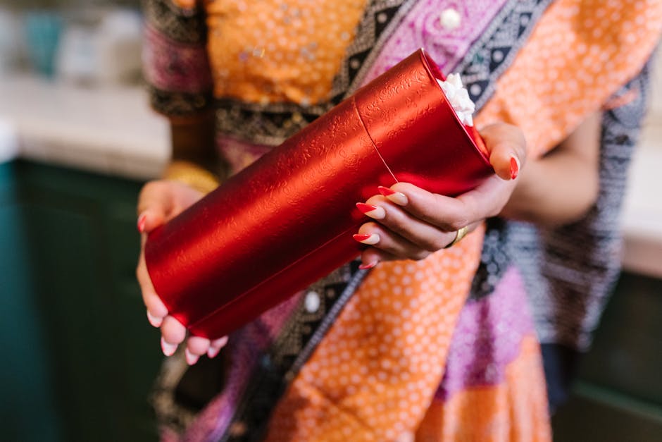 A woman in a colorful sari holds a red gift box during an Indian ceremony.