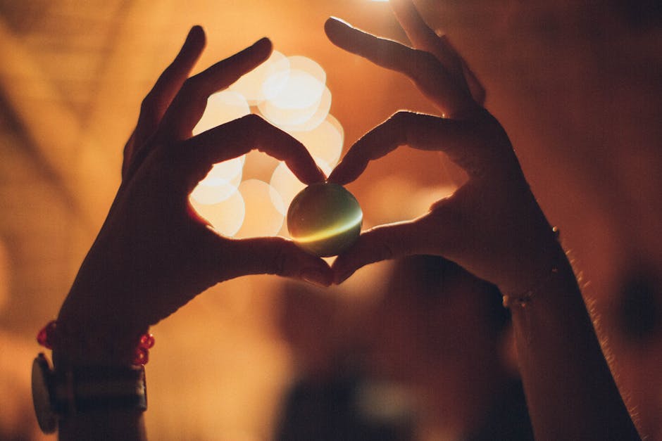 Silhouetted hands form a heart around a glowing orb with warm bokeh background.