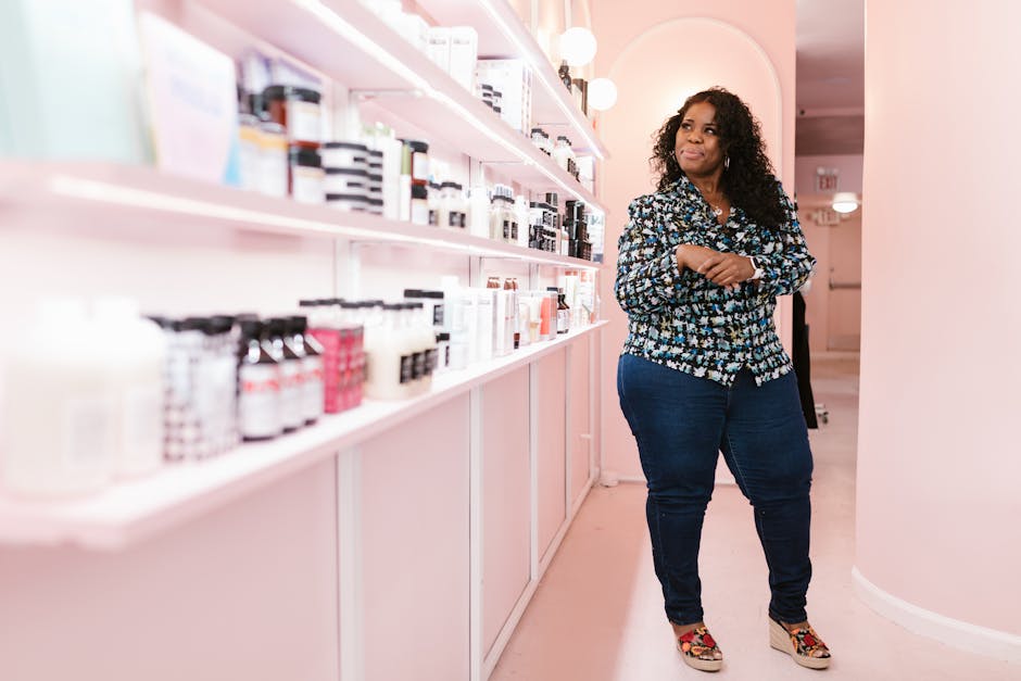 Woman standing in a modern beauty shop, smiling confidently beside shelves of cosmetics.
