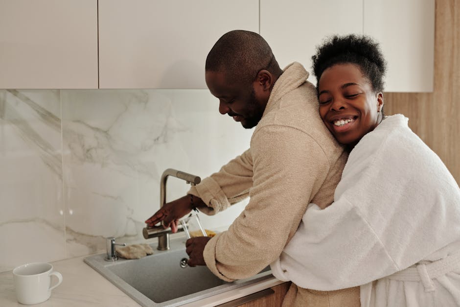 Joyful couple in bathrobes sharing an affectionate hug in a modern kitchen.