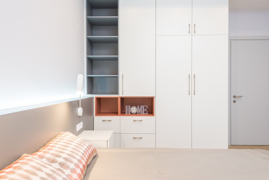 White wardrobe placed near comfortable bed with cushions and bedside table in modern apartment