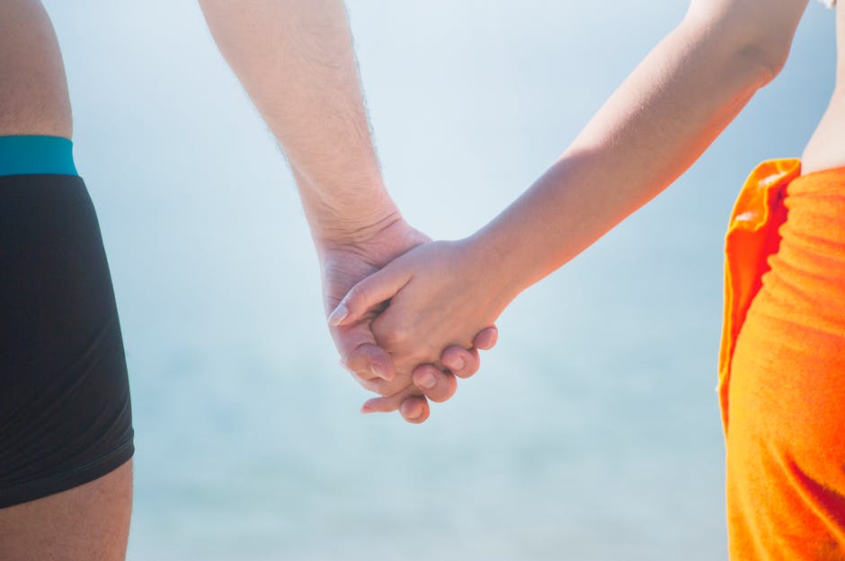 A close-up of a couple holding hands at the beach, symbolizing unity and togetherness.