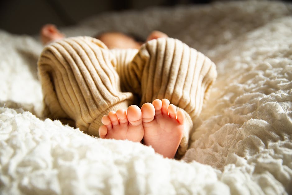 Cute baby sleeping with bare feet visible, in sunlight, on a cozy bed.