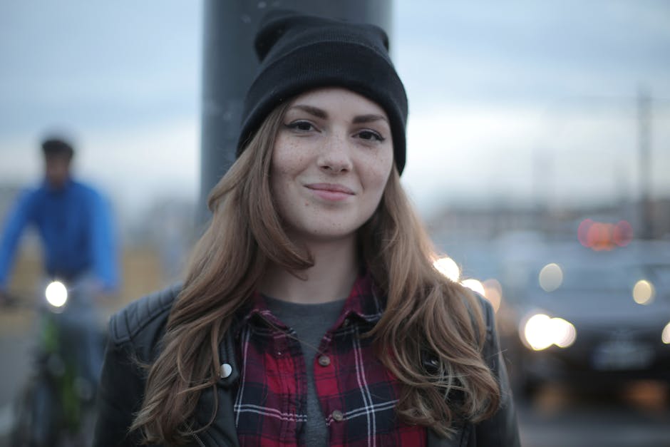 Young woman in a beanie smiling outdoors with urban backdrop, exuding warmth.