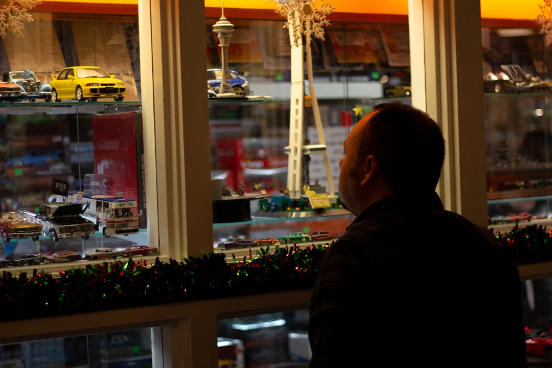 A man looking out a window at a model train set