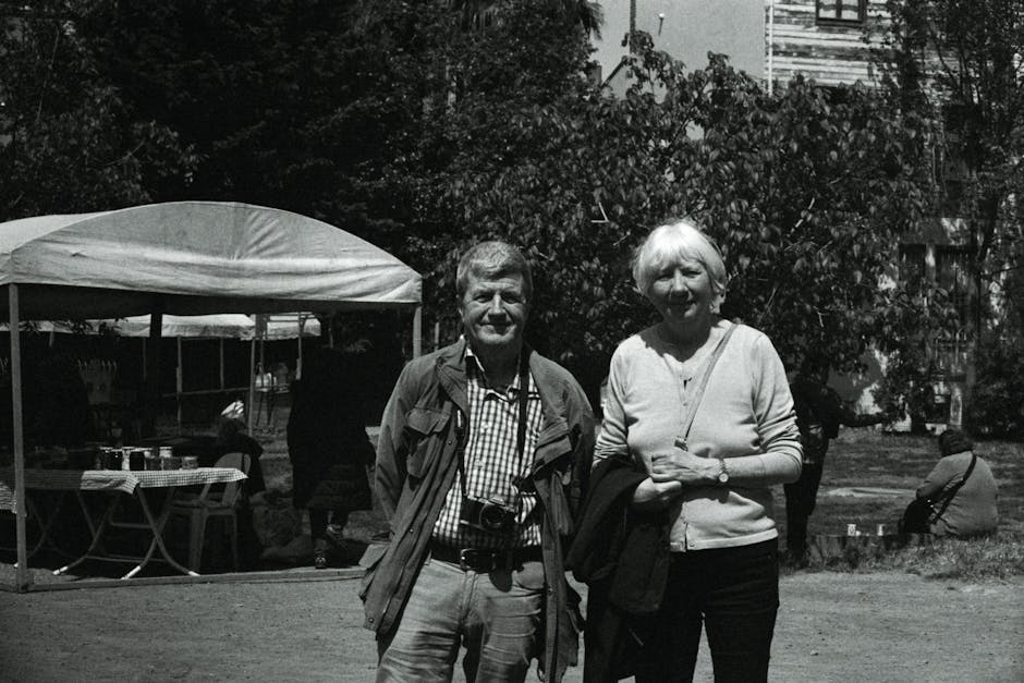 Elderly couple smiling while standing together outdoors in a black and white urban setting.